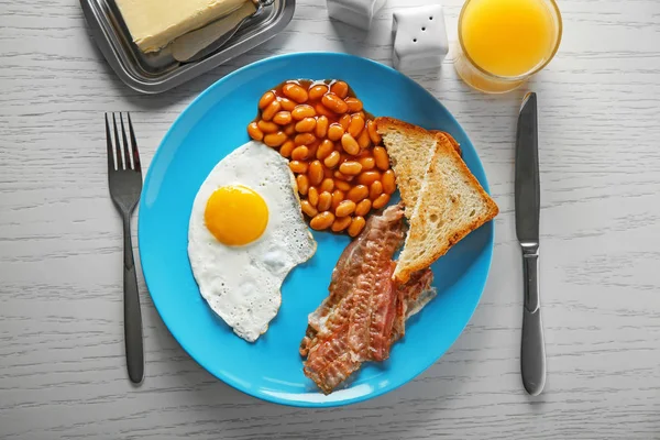 Plate with fried egg, bacon and beans on wooden table