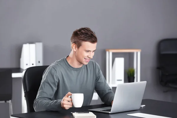 Beau homme avec ordinateur portable et tasse de café au bureau — Photo