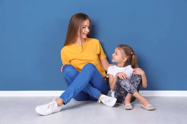 Lycklig mamma och hennes dotter som sitter på golvet mot färg vägg i barnens rum — Stockfoto