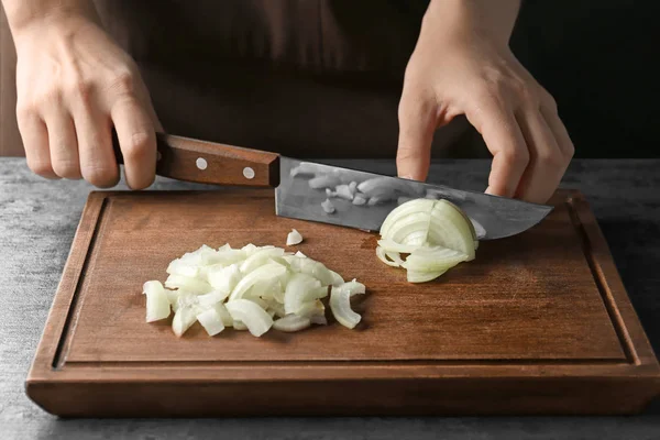 Frau schneidet Zwiebel auf Holzbrett am Tisch — Stockfoto