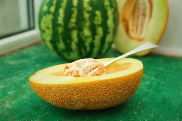 Yummy half of melon and spoon with seeds on wooden table