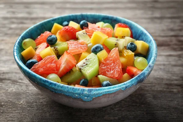 Kom met heerlijke fruitsalade op houten achtergrond — Stockfoto