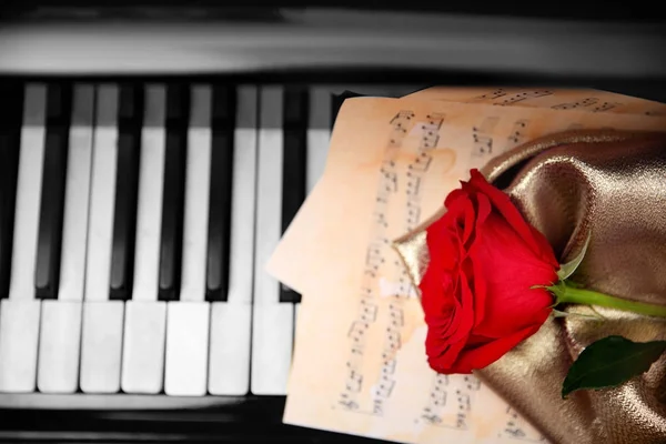 Rode roos en muzikale bladen op piano toetsen — Stockfoto