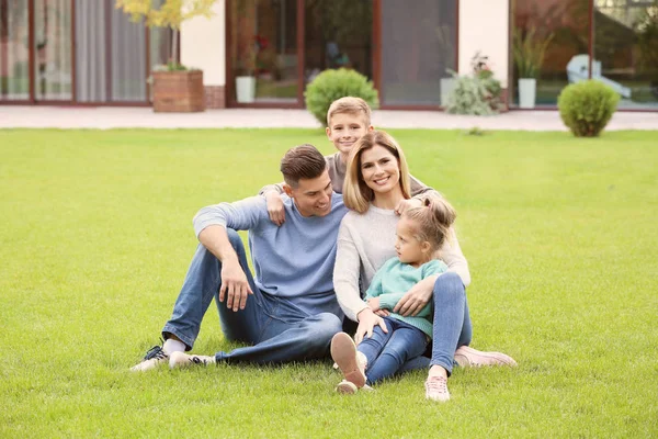 Familia feliz sentado sobre hierba verde en el patio cerca de su casa —  Fotos de Stock