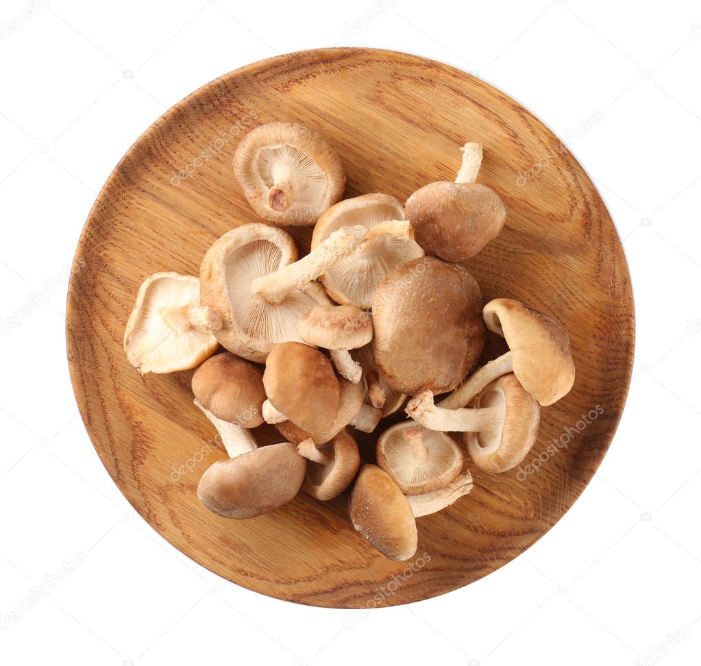 Wooden plate with fresh shiitake mushrooms on white background