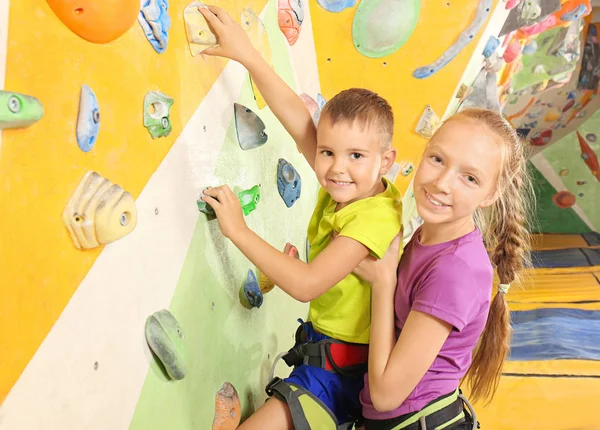 Adorable chica ayudando a su hermano pequeño a subir a la pared en el gimnasio — Foto de Stock