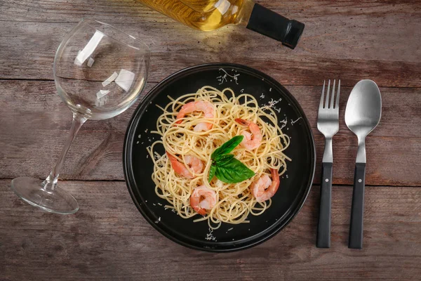 Plate of tasty pasta with shrimps and wine glass on wooden table, top view