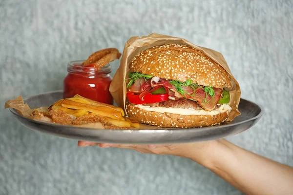 Prosciutto ile lezzetli Burger metal tepsi gri arka plan üzerinde tutan kadın