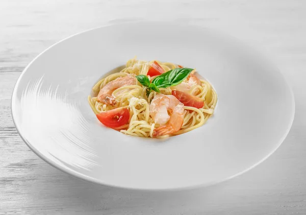 Plate of tasty pasta with shrimps on white wooden table