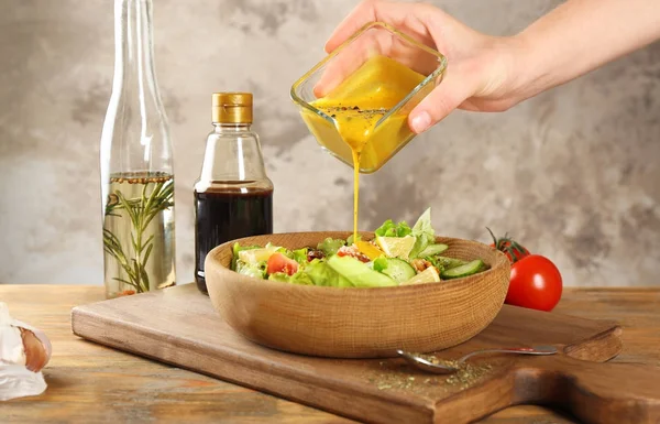 テーブルの上に新鮮なサラダをボウルに蜂蜜マスタードドレッシングを注ぐ女性 — ストック写真