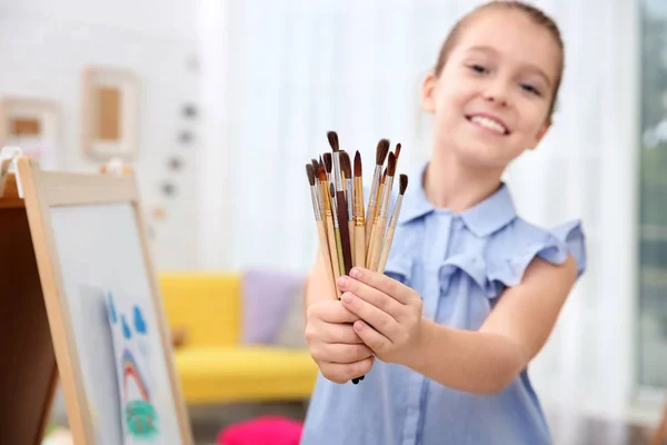 Menina segurando muitos pincéis dentro de casa — Fotografia de Stock