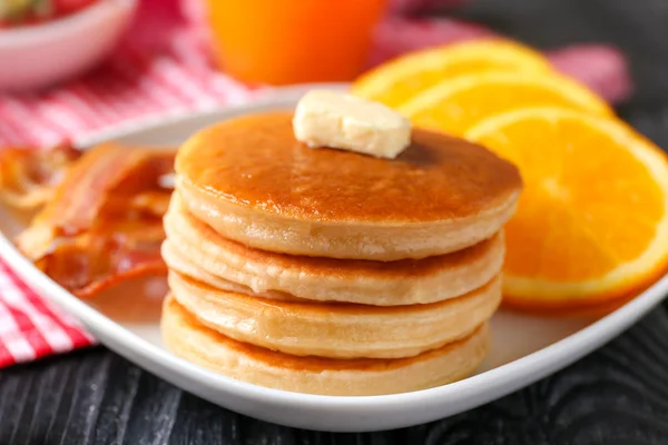 Plate with yummy pancakes, orange and fried bacon on wooden table — Stock Photo, Image