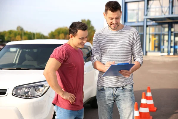 Joven e instructor de conducción de pie cerca del coche — Foto de Stock