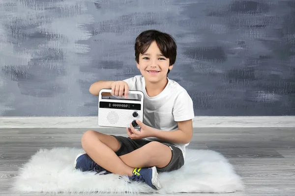 Niño escuchando la radio sentado en el suelo contra la pared gris —  Fotos de Stock