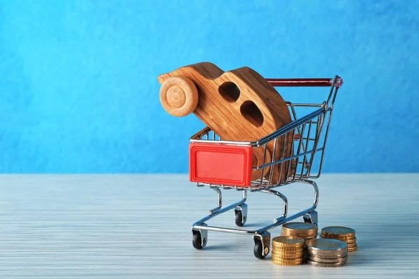 Dřevěné auto v nákupním košíku a mince na stole barvu pozadí — Stock fotografie