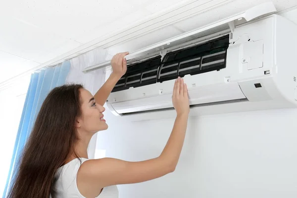 Young woman checking air conditioner at home — Stock Photo, Image