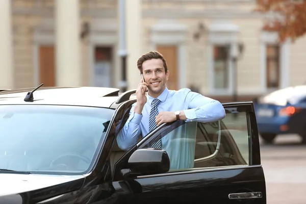Мужчина в формальной одежде разговаривает по телефону возле машины на улице — стоковое фото