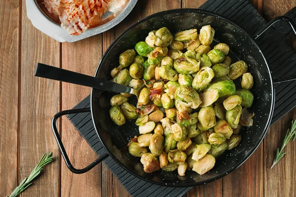 Frying pan with roasted Brussel sprouts and bacon on wooden table — Stock Photo, Image