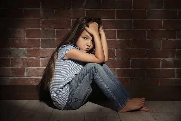 Niña triste sentada en el suelo contra la pared de ladrillo. Abuso del concepto de niños — Foto de Stock
