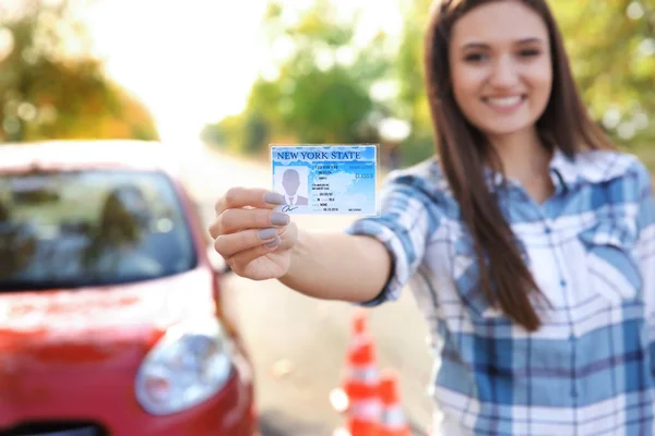 Молода щаслива жінка тримає водійські права біля автомобіля — стокове фото
