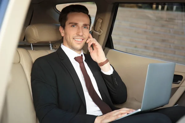 Człowiek w wizytowym z laptopa rozmowy na telefon w samochodzie — Zdjęcie stockowe