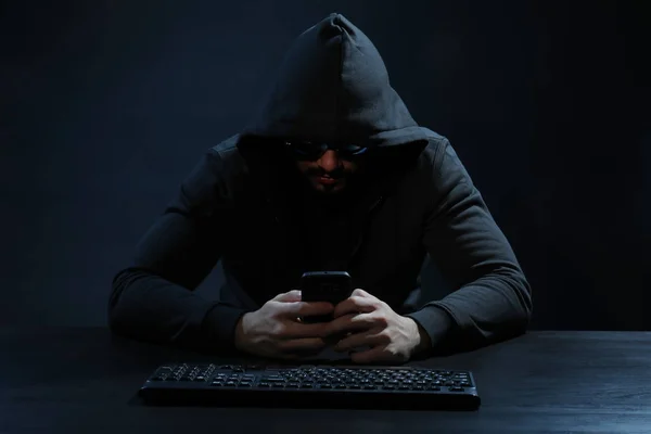 Hacker met telefoon op donkere achtergrond — Stockfoto