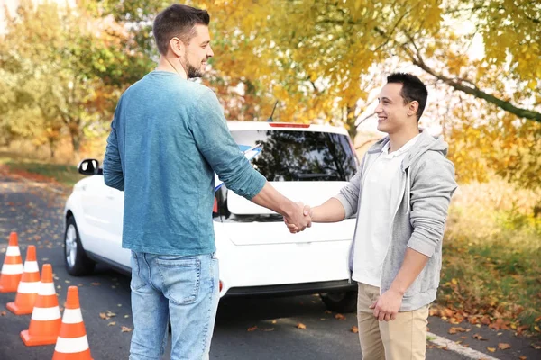 Instruktor a mladý muž předán řidičský průkaz zkouška, venku — Stock fotografie