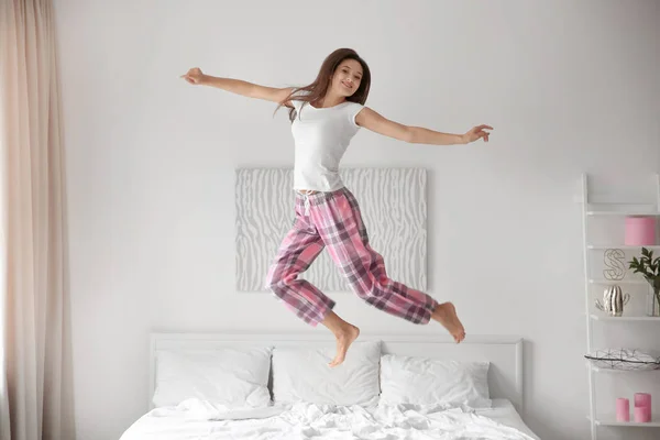 Young woman jumping on bed at home