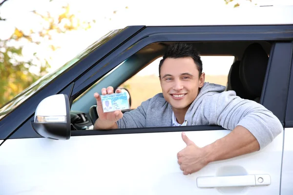 Young man holding driving license in car