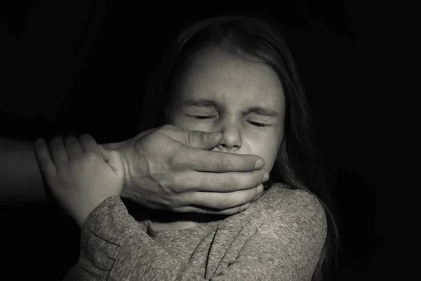 Man's hand covering mouth of little girl on black background. Abuse of children concept — Stock Photo, Image