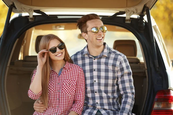 Belo jovem casal sentado no porta-malas do carro — Fotografia de Stock