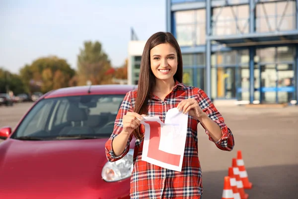 Feliz joven mujer desgarrando aprendiz conductor signo cerca de coche —  Fotos de Stock