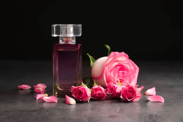 Бутылка духов и роз на темном фоне — стоковое фото