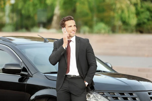 Hombre en ropa formal hablando por teléfono cerca de coche al aire libre — Foto de Stock