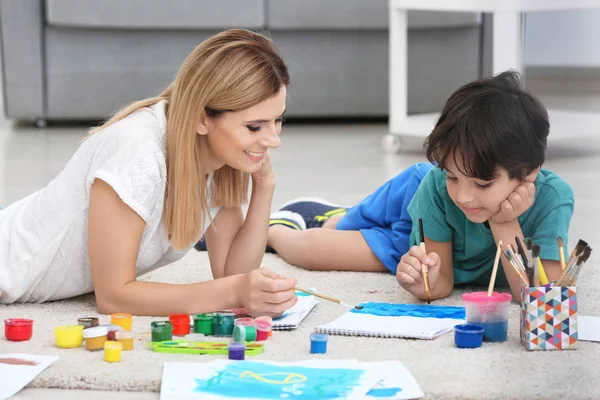 Mother with son painting while lying on floor at home