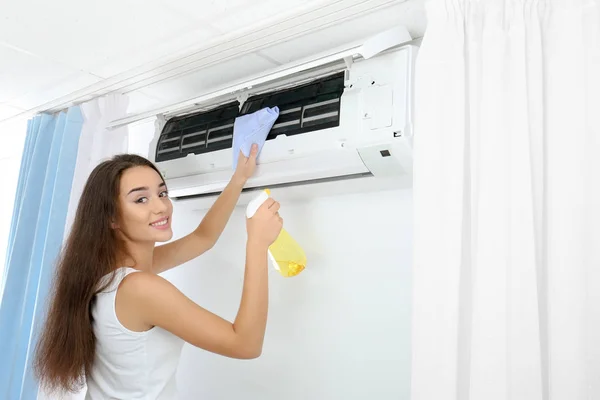 Young woman cleaning air conditioner at home