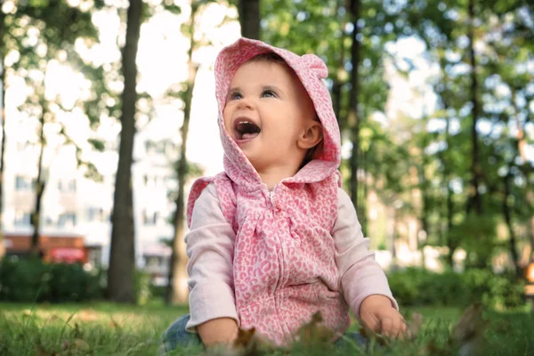 Adorable little girl sitting on grass in autumn park — Stock Photo, Image