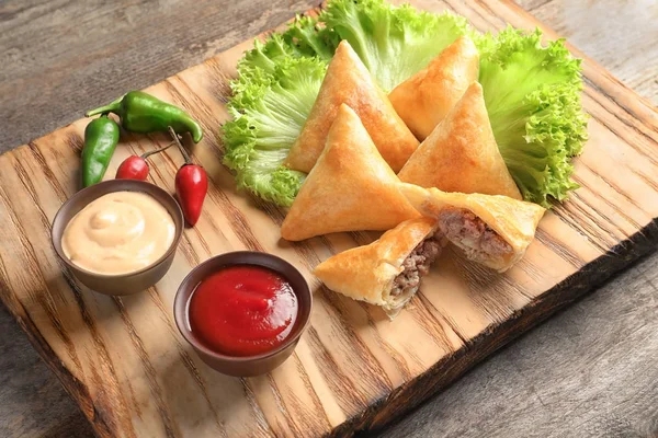 Placa de madeira com deliciosas samosas de carne na mesa — Fotografia de Stock