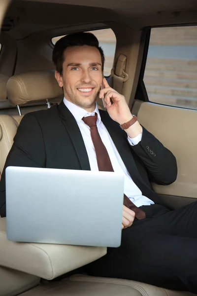 Uomo in abito formale con laptop che parla al telefono in auto — Foto Stock