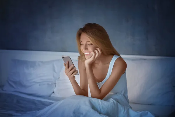 Vacker ung kvinna med mobiltelefon i sängen på natten — Stockfoto