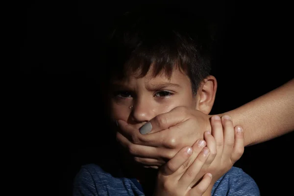 Female hand covering mouth of little boy on black background. Abuse of children concept