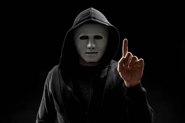 Хакер в маске нажимает кнопку на виртуальном экране на темном фоне — стоковое фото