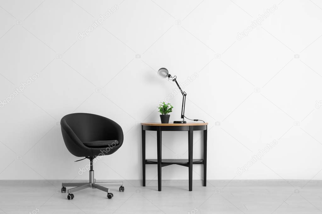 Comfortable armchair and table near light wall