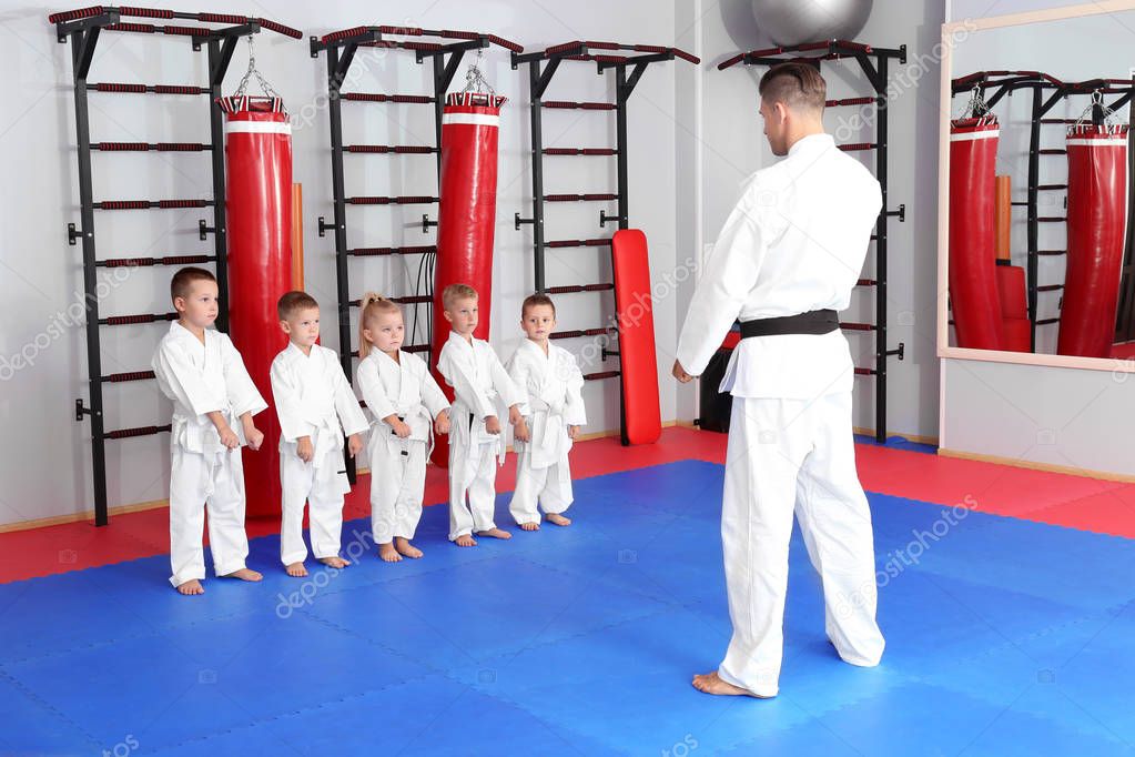 Male karate instructor training little children in dojo