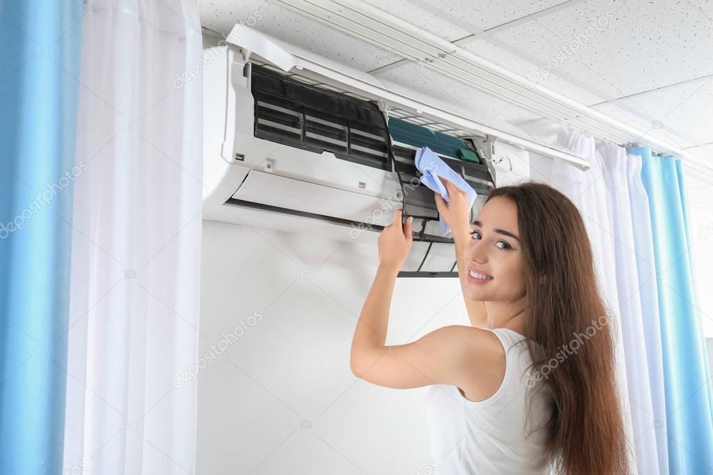 Young woman cleaning air conditioner at home