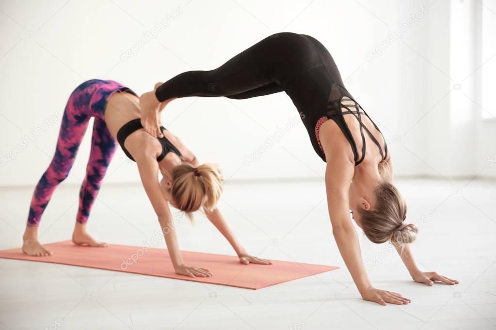 Two young women practicing yoga in light room