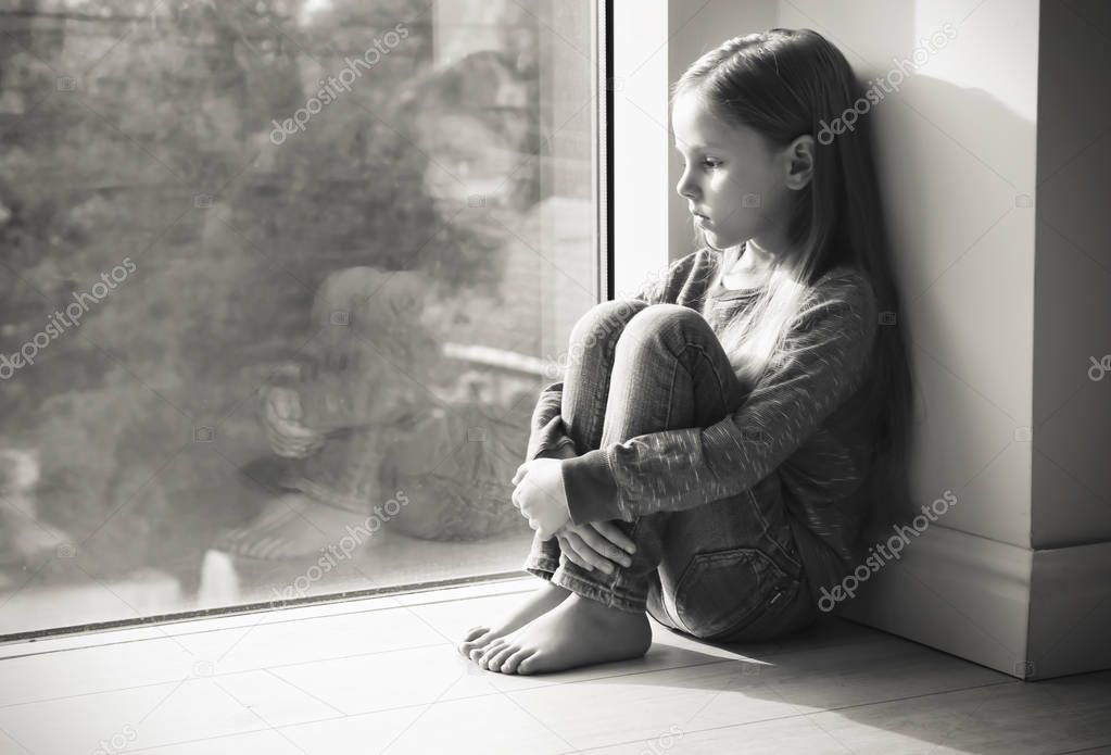 Little sad girl near window. Abuse of children concept