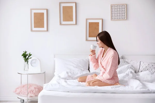 Mladá žena, pití kávy, zatímco sedí na posteli doma — Stock fotografie