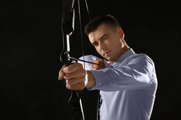 Jovem empresário praticando tiro com arco em fundo escuro — Fotografia de Stock