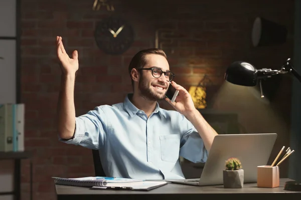 Young man with laptop and cell phone in office at night — Stock Photo, Image